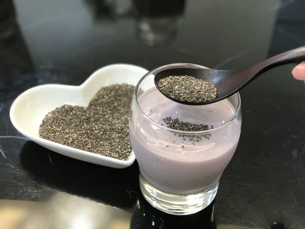 Adding a Spoonful of Chia Seeds to a Glass of Yogurt