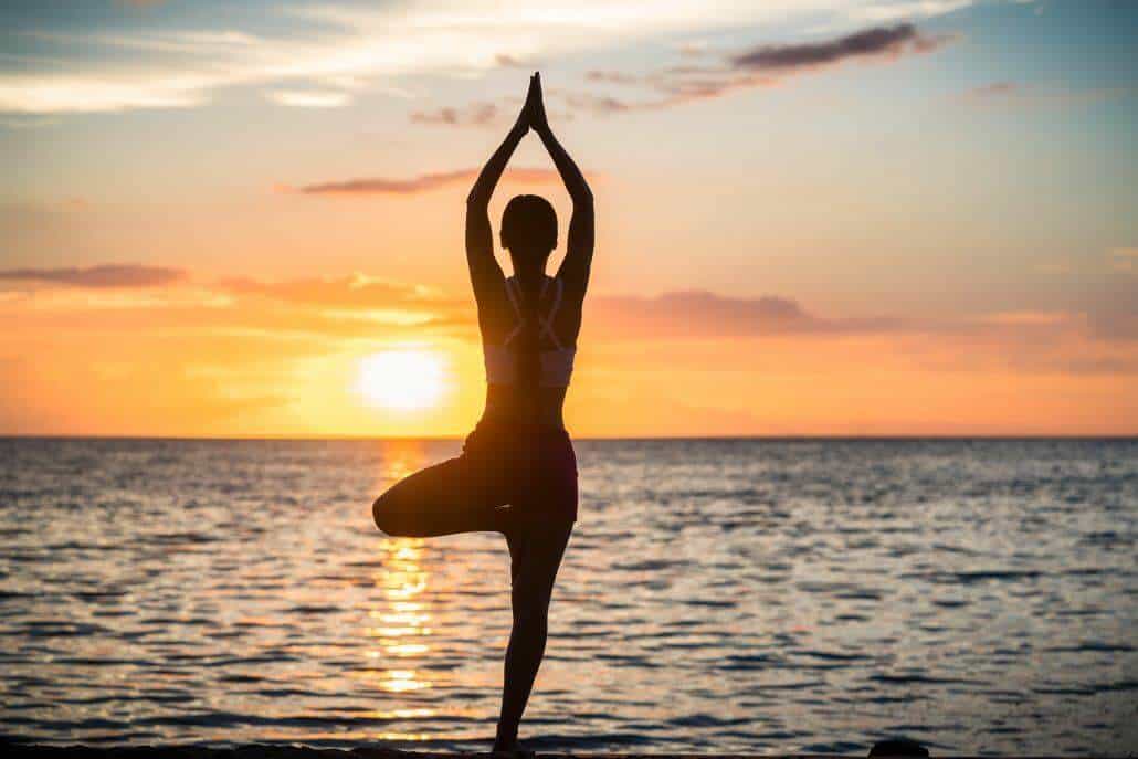 Woman doing yoga by the sea facing the sunset 