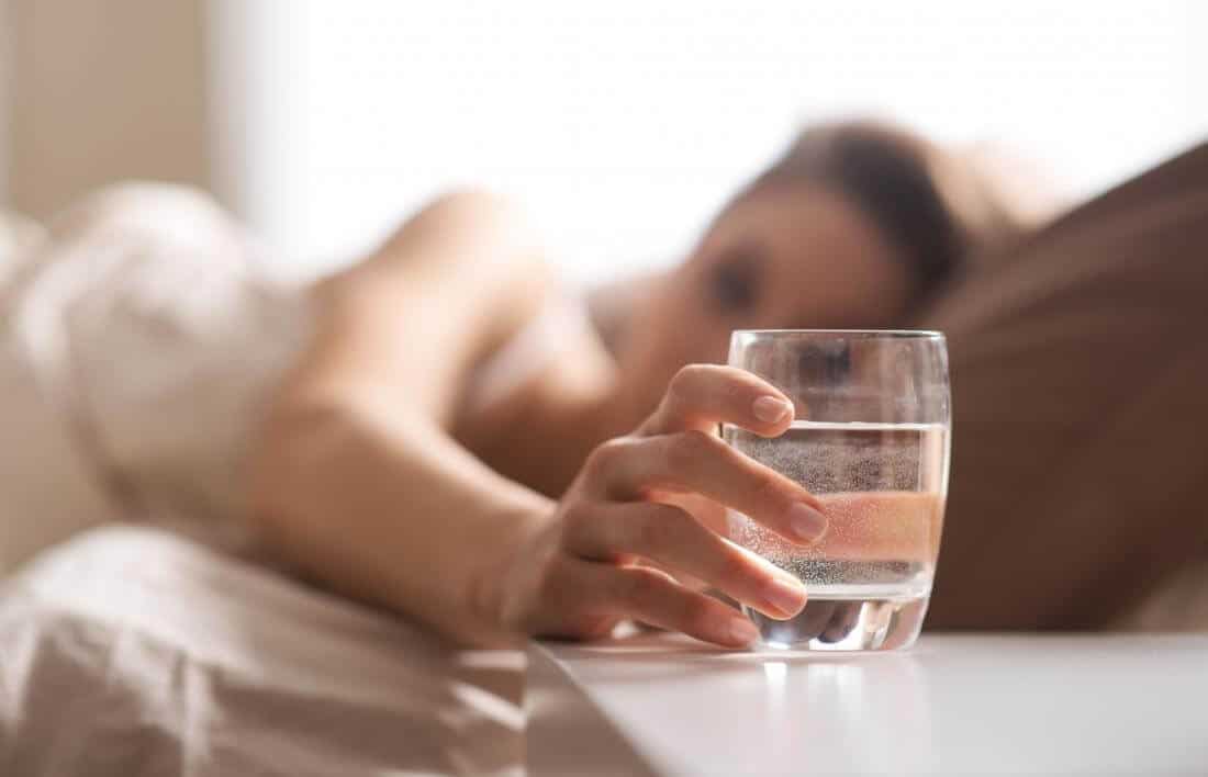 Woman in bed grabbing a glass of water on the bedside table
