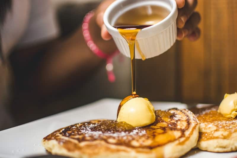 pouring honey over a stack of pancakes