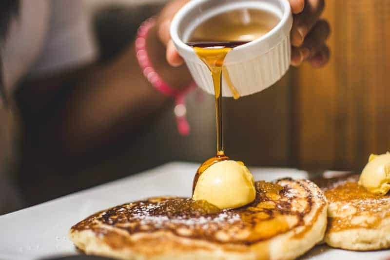 pouring honey over a stack of pancakes