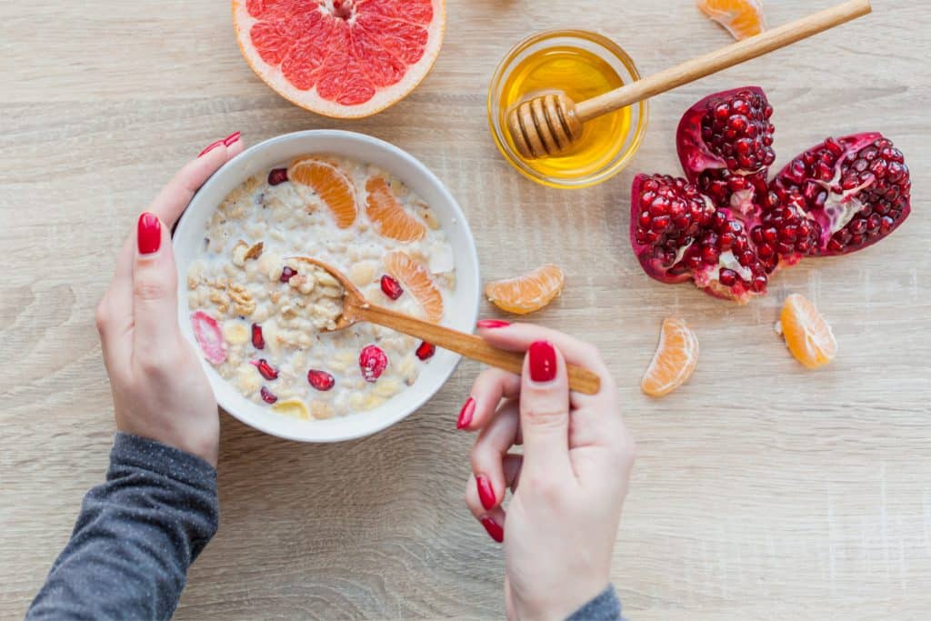 adding honey into a bowl of oats with pomegranate seeds