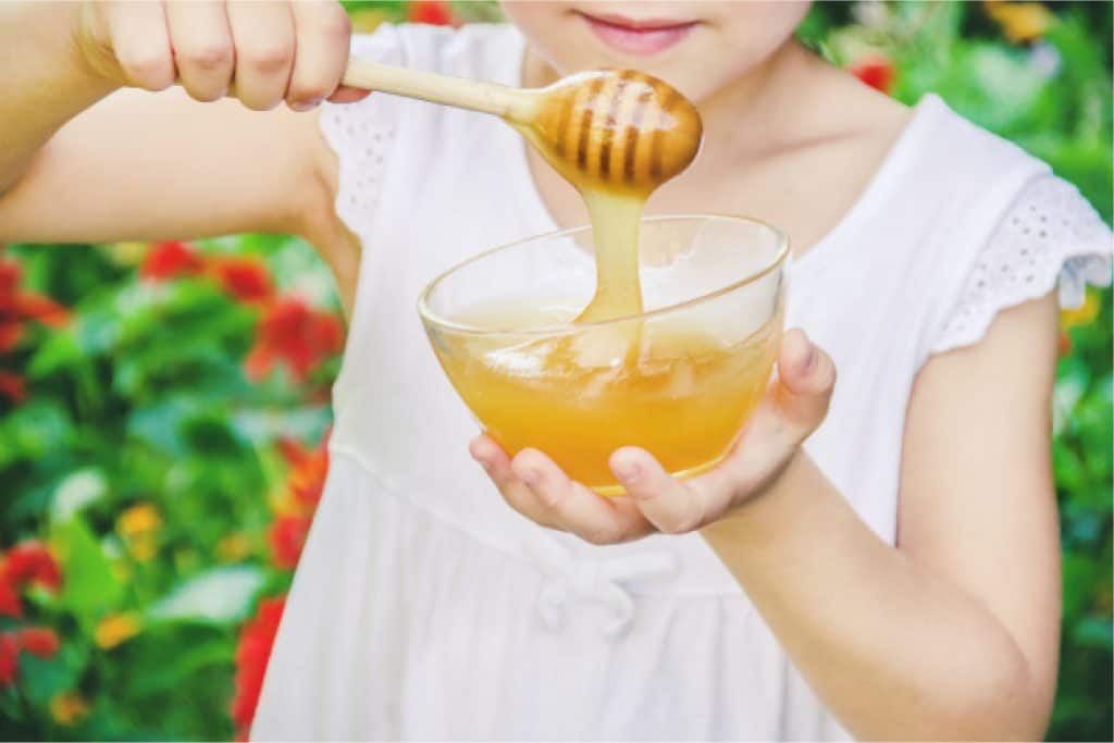 Child using a honey dipper to scoop up honey from a bowl
